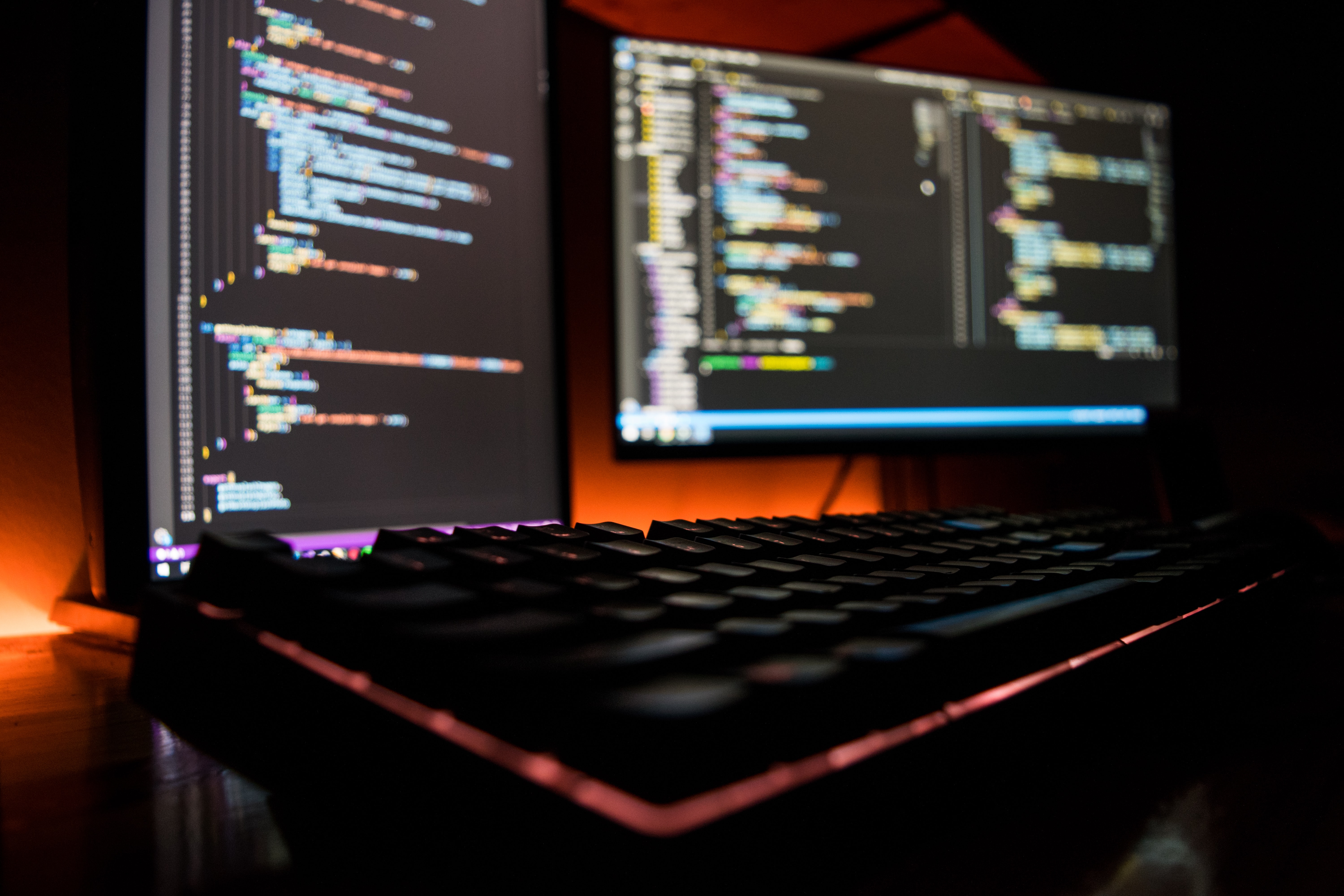 Dois monitores com código escrito em uma linguagem de programação na tela e um teclado mecânico